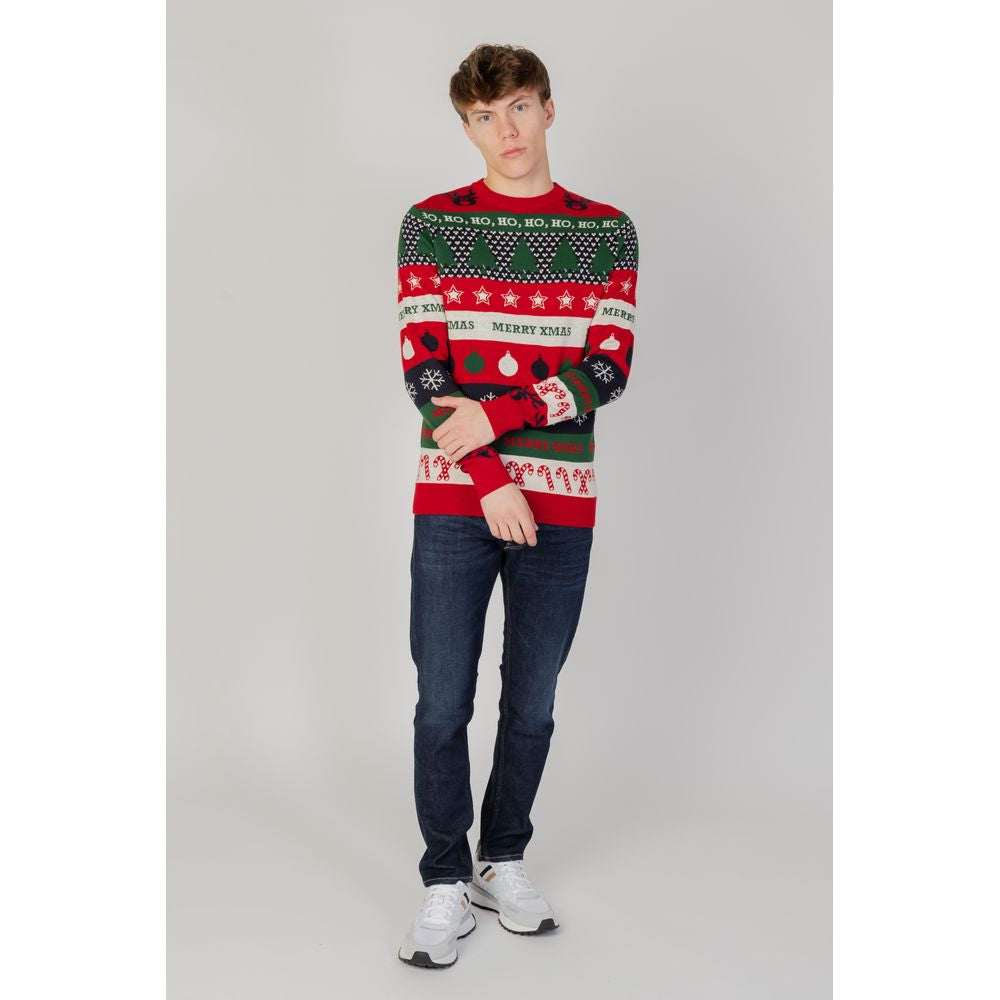 Model wearing festive red and green Christmas sweater with text and patterns, paired with dark jeans and white sneakers.