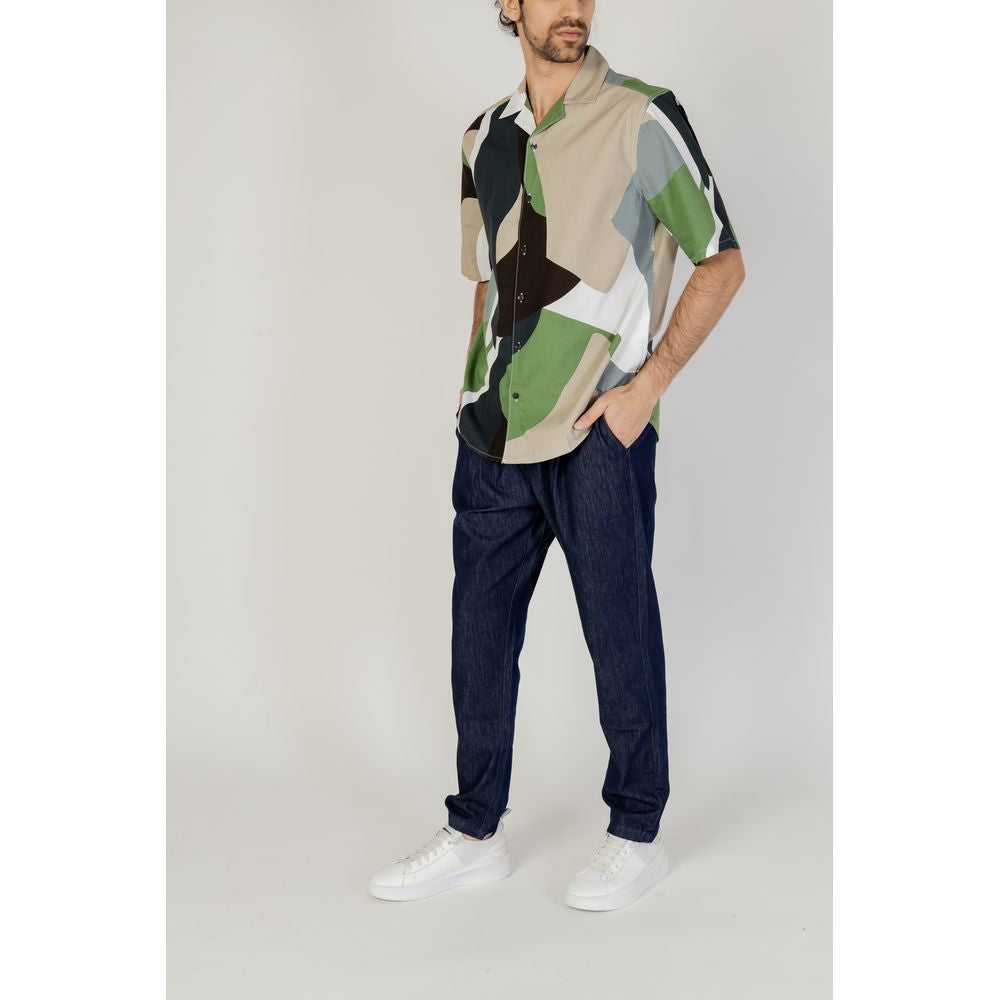 Model wearing Only & Sons green cotton shirt with short sleeves, part of spring/summer collection, paired with blue jeans and white sneakers.