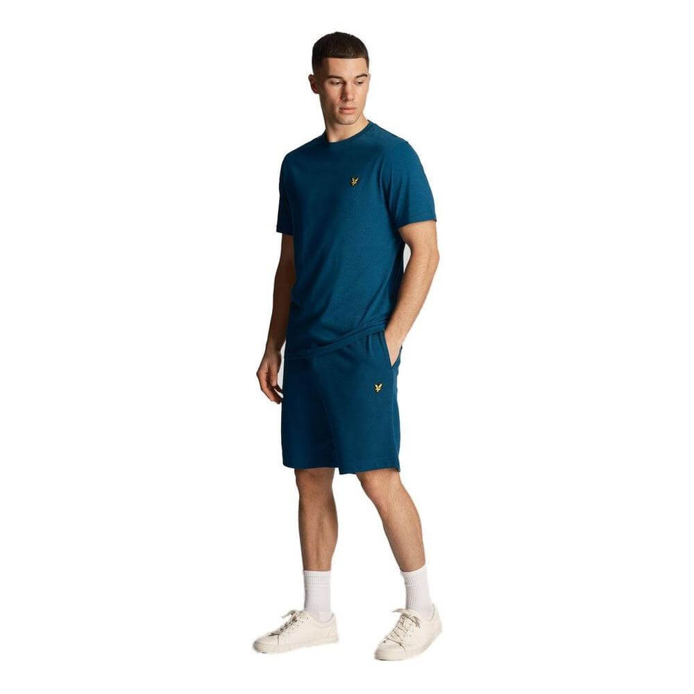 Man wearing Lyle & Scott teal cotton bermuda shorts set, featuring the iconic eagle logo, part of the Fall/Winter collection.