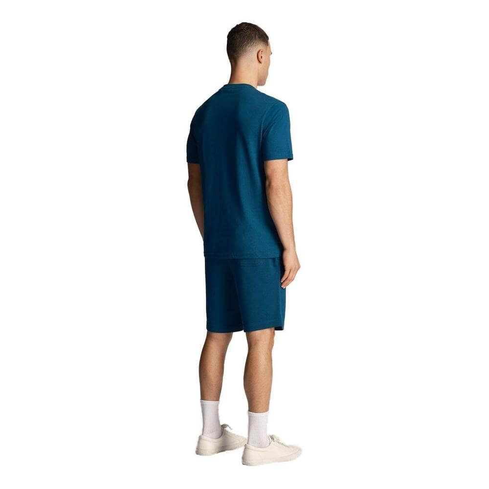 Back view of a man wearing a matching blue t-shirt and shorts set, paired with white sneakers, against a plain background.