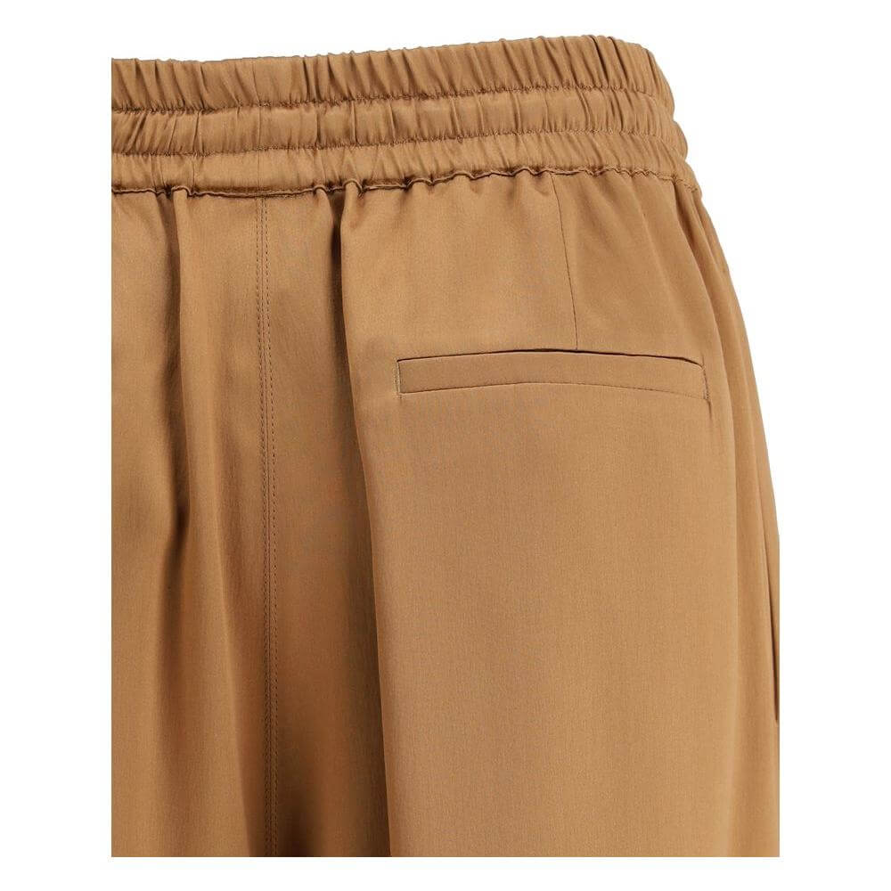 Close-up of Dolce & Gabbana satin pajama pants showing elasticated waistband and back welt pocket in a luxurious tan fabric.
