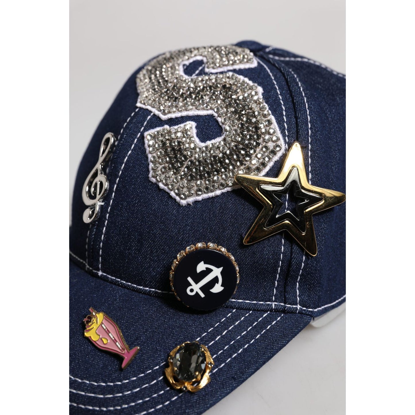 Dolce & Gabbana blue baseball cap with crystal embellishments, star, and anchor details on denim fabric.
