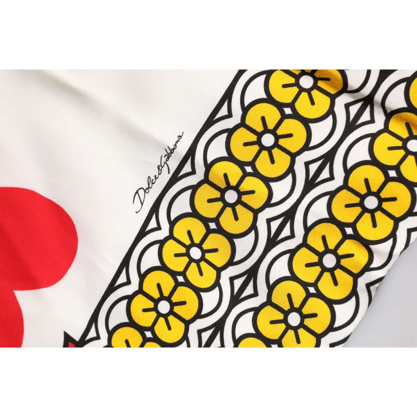 Close-up of Dolce & Gabbana Maxi Dress fabric showing white background with yellow floral and heart patterns. Signature visible.