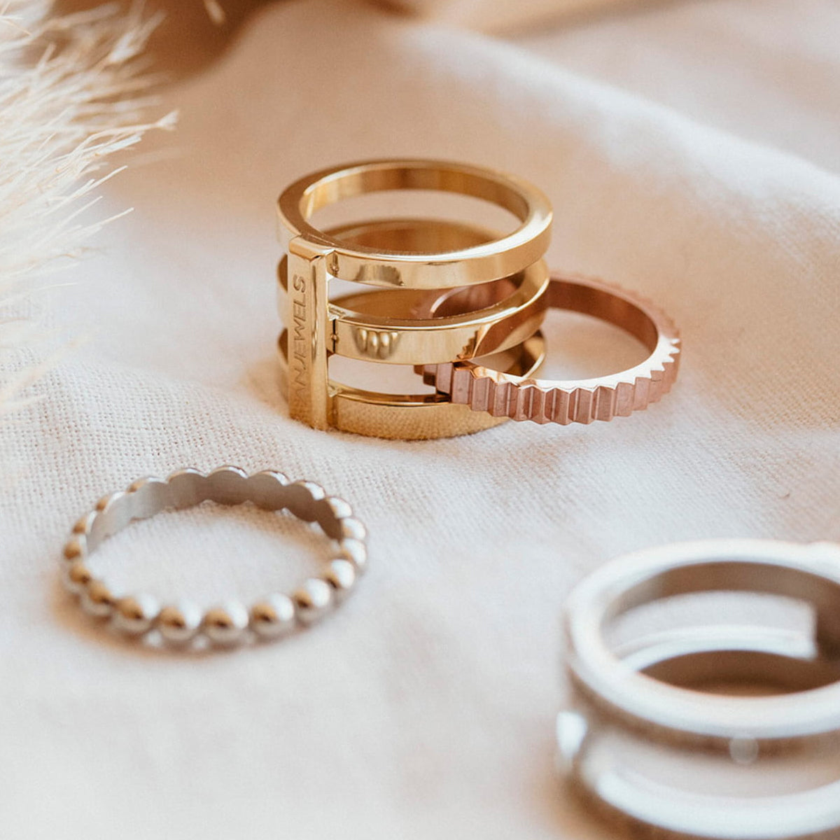 Stack of elegant rings featuring AN JEWELS JEWELRY Mod. AR.R1NS05R-8 in gold and silver tones on a soft fabric surface.