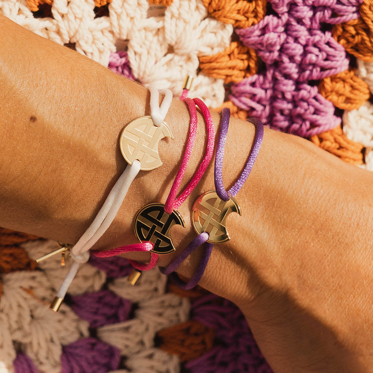 Three colorful AN JEWELS JEWELRY Mod. AV.BGLBGGPK bracelets on wrist against crochet background.