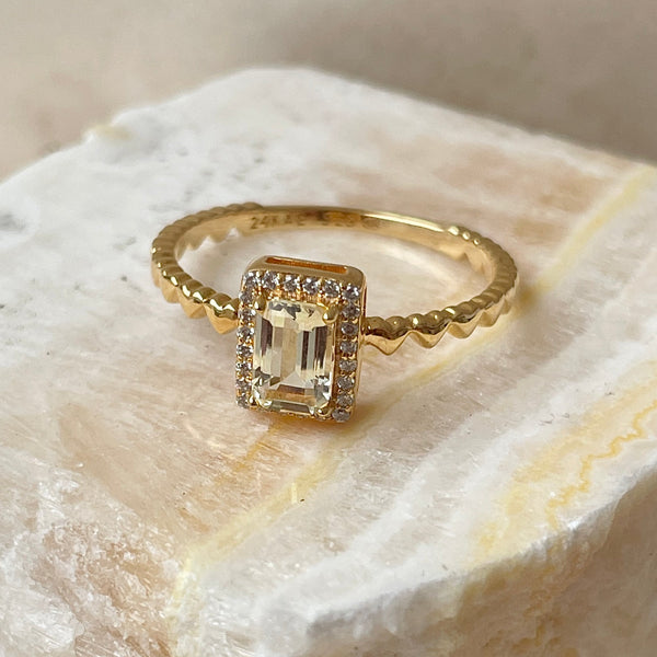 24KAE JEWELS JEWELRY Mod. 12472Y/52 featuring a gold ring with a rectangular gemstone and diamond accents, displayed on a light stone surface.