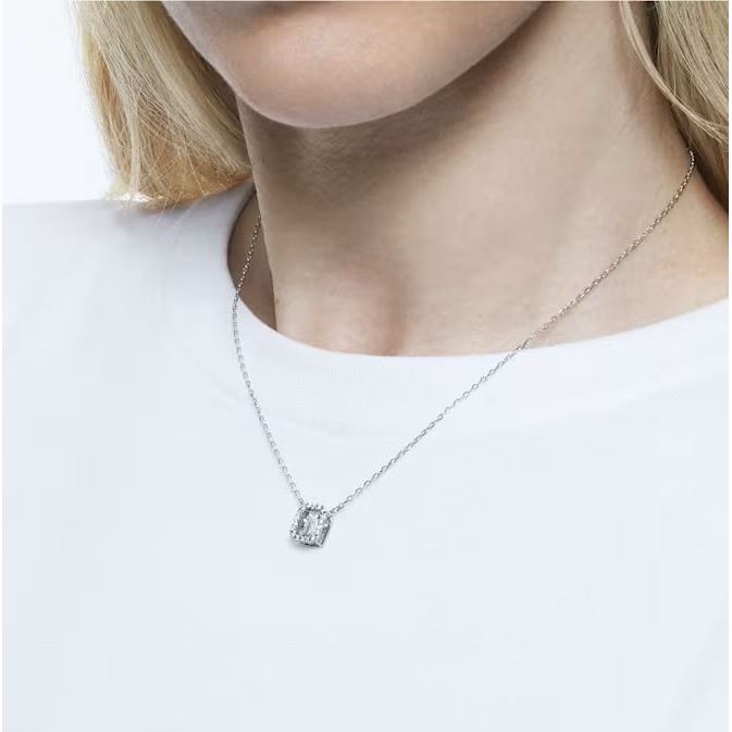 Woman wearing a silver necklace with a square pendant, shown on a white shirt.