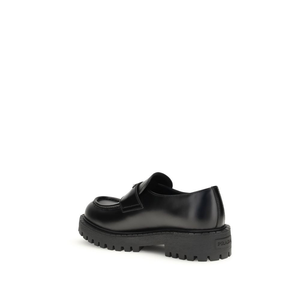 Prada Black Calf Leather Bos Taurus Slip-On Loafers with rubber sole, side view showing craftsmanship and enameled metal triangle detail.