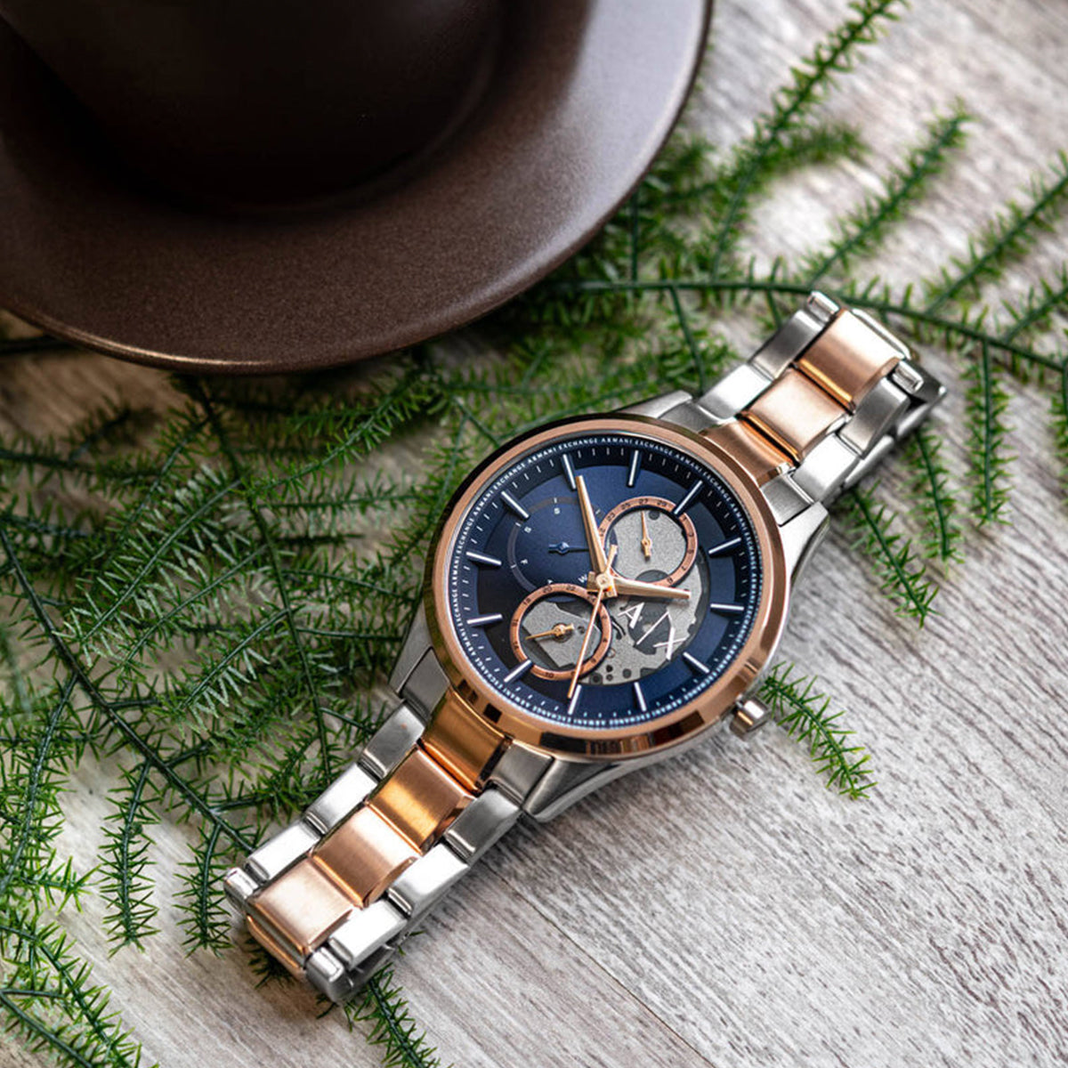 ARMANI EXCHANGE Mod. AX1874 wristwatch with SS IP rose gold case, quartz movement, and mineral dial, displayed on a wooden surface with foliage.