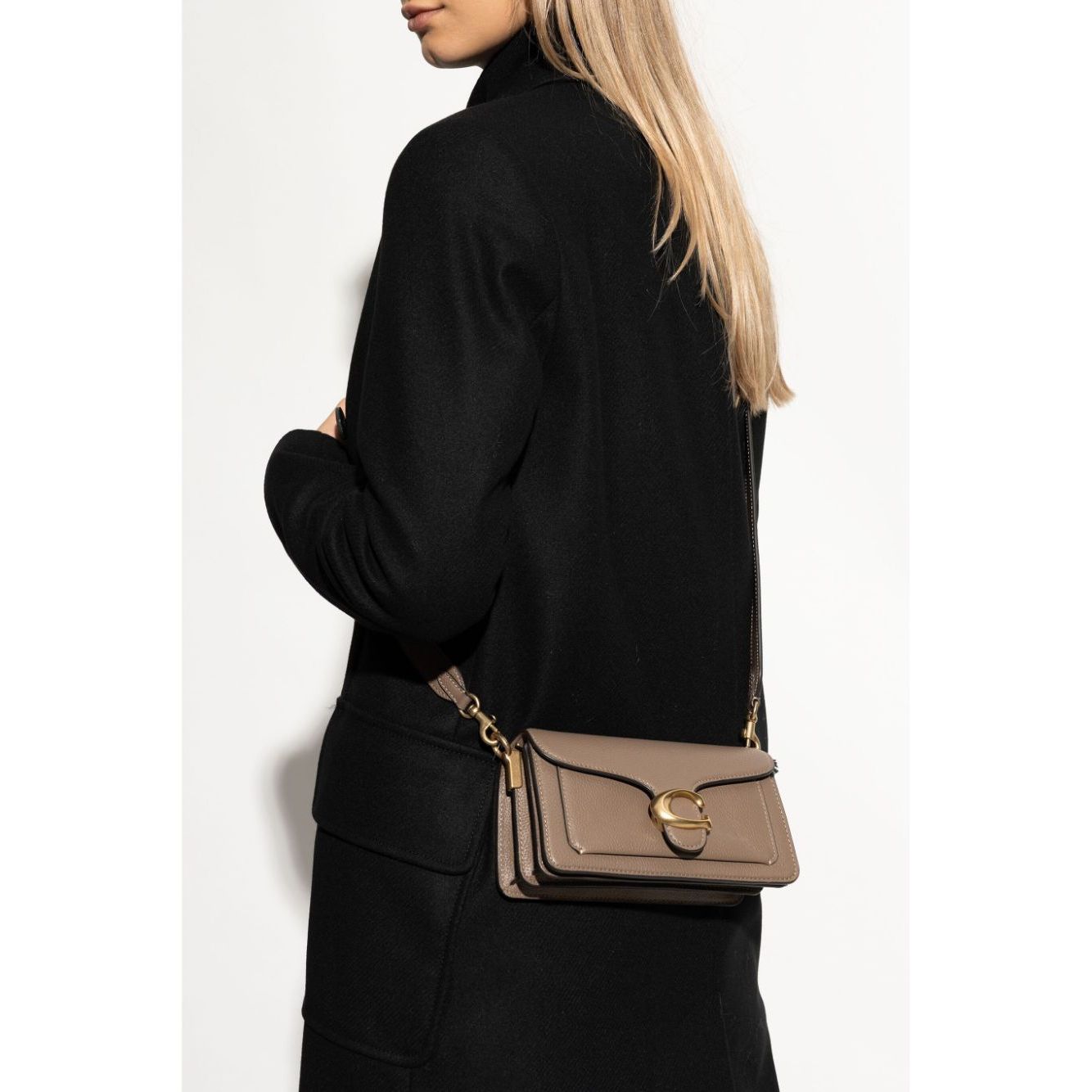 Woman wearing black coat with Coach Tabby 20 shoulder bag, leather crossbody featuring multifunctional pockets and removable strap.