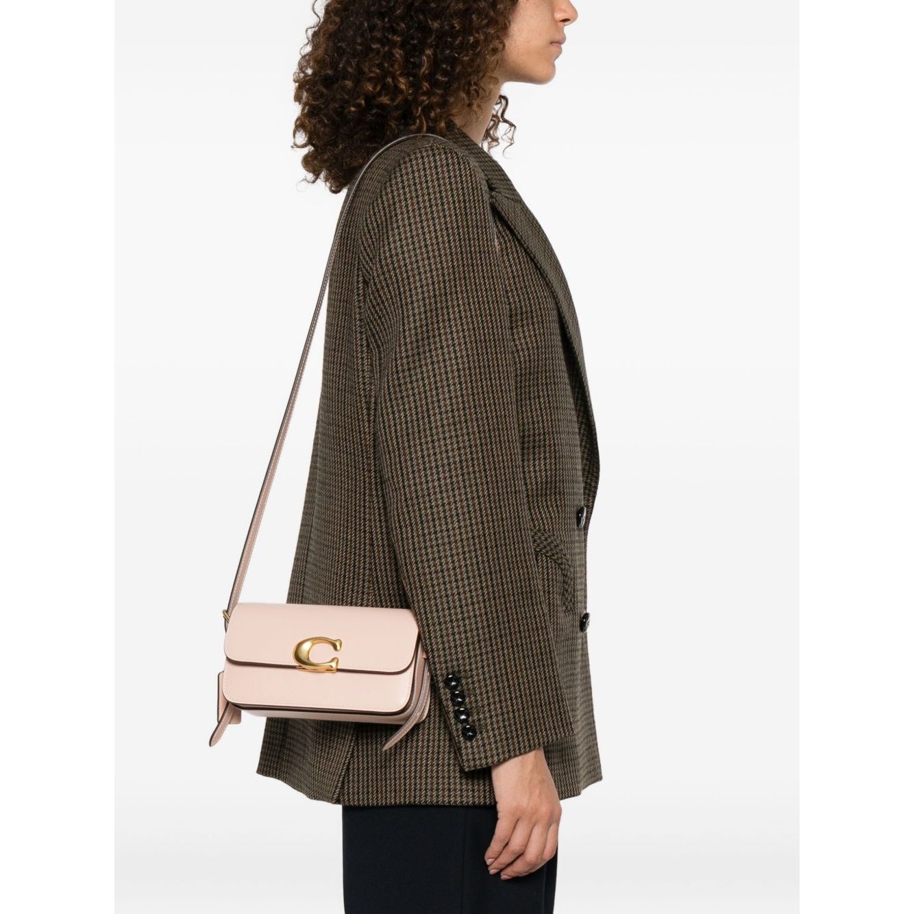 Woman wearing a cream Coach Zoe leather shoulder bag with gold-tone clasp, featuring a shoulder strap and rectangular shape, side view.